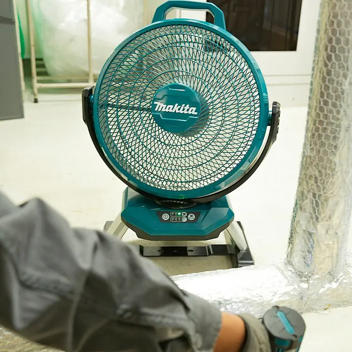 Makita LXT 18V Akku-Ventilator DCF301Z - 18 V, Ohne Akku - Ein tealfarbener Makita-Ventilator auf einem Werkstattboden, dessen Bedienfeld mit beleuchteten Anzeigen sichtbar ist.