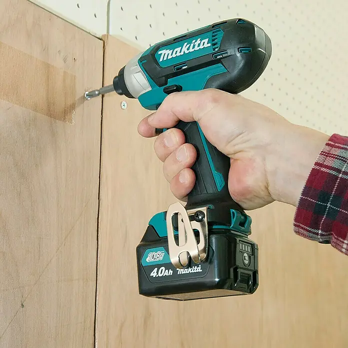Makita Akku-Schlagschrauber TD110DSMJ - 10,8 V, 2 Akkus, 4 Ah - Eine Hand hält einen schwarz-türkisen Makita Schlagschrauber mit 10.8V 4.0Ah Akku, der eine Schraube in eine helle Holzplatte treibt.