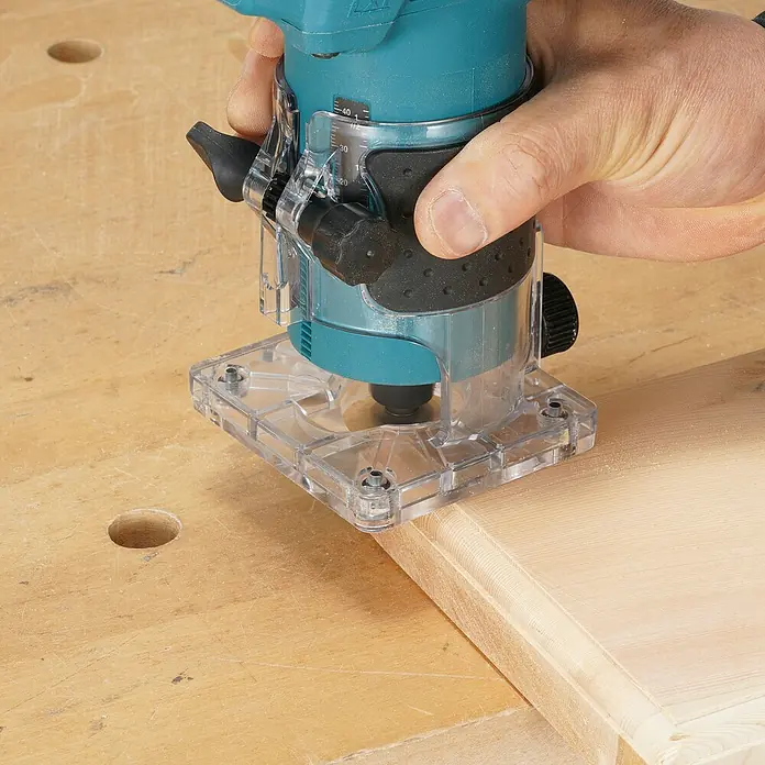 Makita LXT 18V Akku-Kantenfräser DRT52Z - 18 V, Ohne Akku, Leerlaufdrehzahl: 30.000 U/min - Hand führt eine türkise und durchsichtige Kantenfräse, um eine Zierkante an einem Holzbrett zu fräsen.