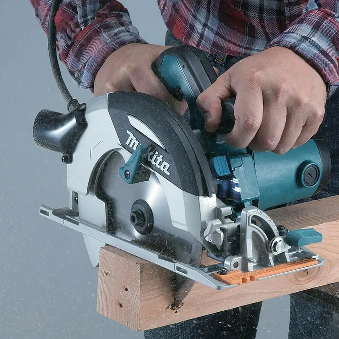 Makita Handkreissäge HS7101J1 - 1.400 W, Durchmesser Sägeblatt: 190 mm - Eine Person verwendet eine türkis-silberne Makita Handkreissäge zum Sägen eines Holzstücks, mit Sägespänen in der Luft.