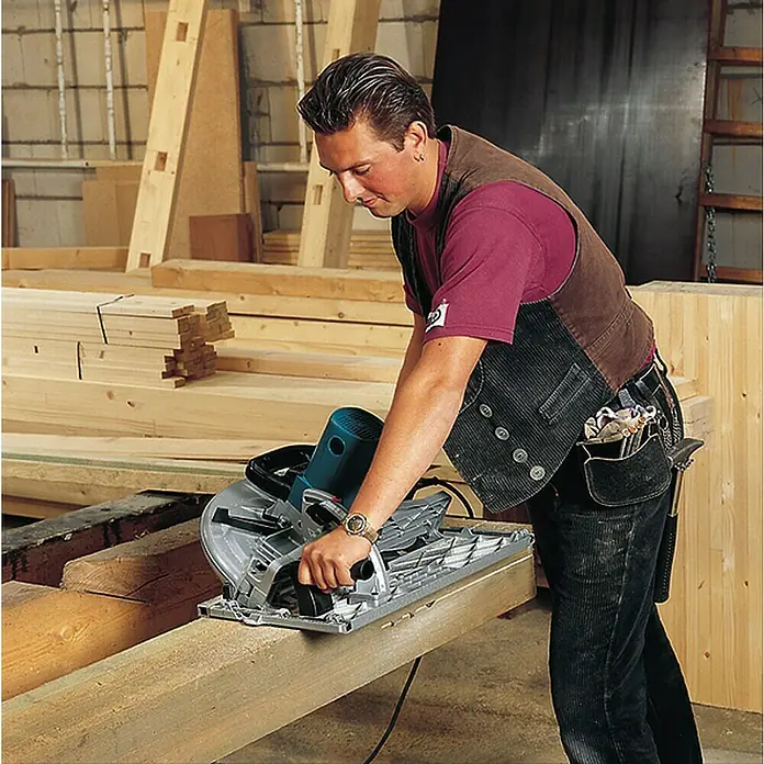 Makita Handkreissäge 5143R - 2.200 W, Durchmesser Sägeblatt: 355 mm, Schnitttiefe bei 90 °: 130 mm - Mann benutzt eine blau-silberne Kreissäge, um einen Holzbalken zu sägen.