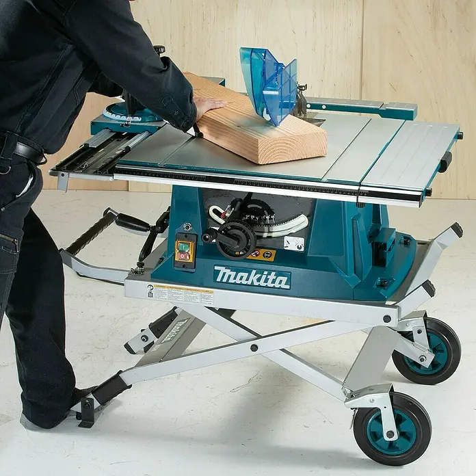 Makita Tischkreissäge MLT100NX1 mit Untergestell - 1.500 W, Durchmesser Sägeblatt: 260 mm, Schnitttiefe bei 90 °: 93 mm - Eine Person bedient eine türkisfarbene und silberne Makita Tischkreissäge mit Rollgestell, die ein Holzstück schneidet.