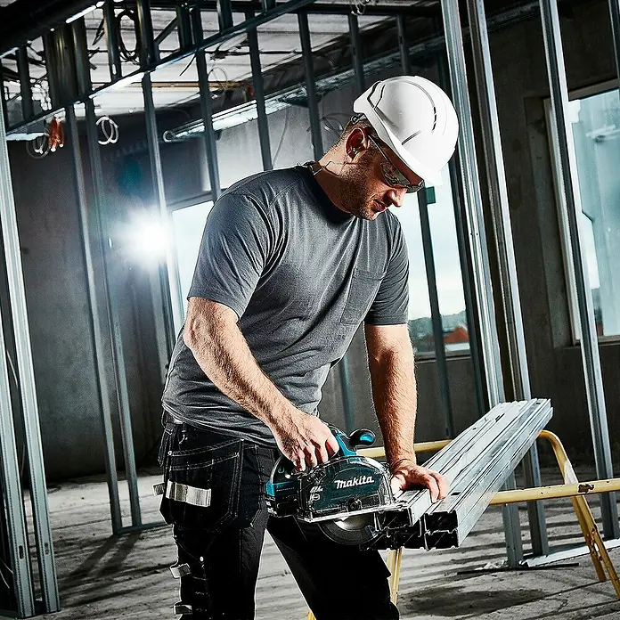 Makita LXT 18V Akku-Handkreissäge DCS553RTJ - 18 V, 2 Akkus, 5 Ah - Ein Bauarbeiter schneidet Metallständer mit einer türkisfarbenen und schwarzen Makita Kreissäge auf einer Baustelle.