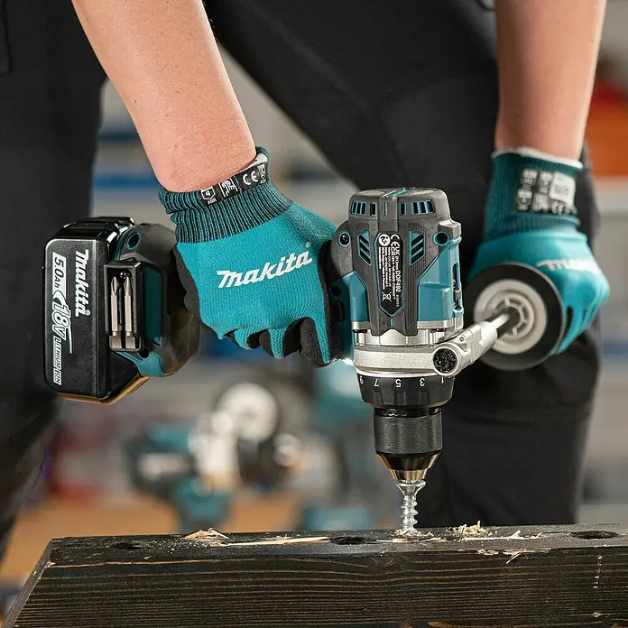 Makita LXT 18V Akku-Bohrschrauber DDF492RTJ - 18 V, 2 Akkus, 130 Nm - Eine Person mit türkisfarbenen Handschuhen verwendet einen Makita Akku-Bohrschrauber, um eine Schraube in einen dunklen Holzbalken zu befestigen.
