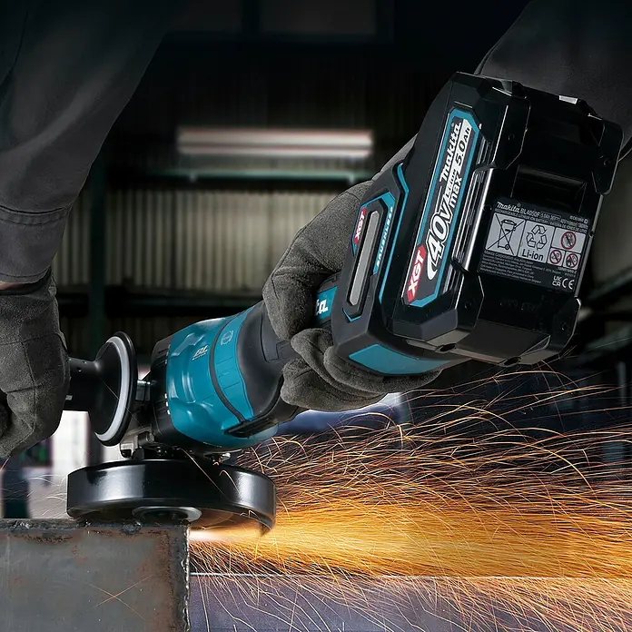 Makita XGT 40V max. Akku-Winkelschleifer GA050GZ - Ohne Akku, Durchmesser Scheibe: 125 mm - Makita Akku-Winkelschleifer mit 40V XGT Akku, von behandschuhten Händen gehalten, schleift Metall und erzeugt helle Funken.