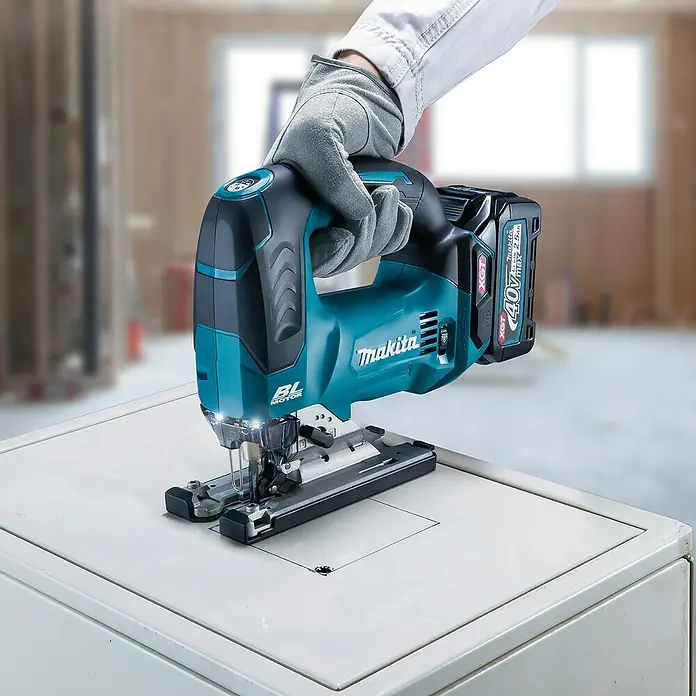 Makita XGT 40V max. Akku-Pendelhubstichsäge JV002GZ - 40 V, Ohne Akku, 0 /min - 3.500 /min - Behandschuhte Hand nutzt türkise/schwarze Makita Akku-Stichsäge, um in weiße Oberfläche zu schneiden. Mit 40V max 2.5Ah Akku.