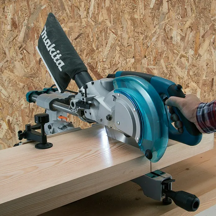 Makita Kapp- & Gehrungssäge LS0815FLN - 1.400 W, Durchmesser Sägeblatt: 216 mm, 0 U/min - 5.000 U/min - Eine Person benutzt eine blau-silberne Makita Kapp- und Gehrungssäge, um ein helles Holzbrett zu schneiden.