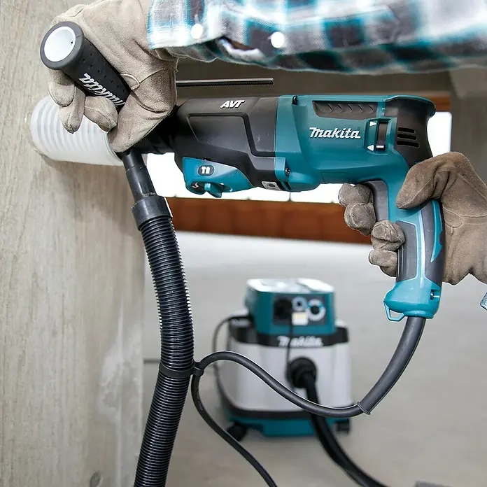 Makita Kombihammer HR2631FT13 - 800 W, 2,4 J, Schnellspannbohrfutter - Eine Person bohrt mit einem türkis-schwarzen Makita Bohrhammer und Staubabsaugung in eine Betonwand, verbunden mit einem passenden Sauger.