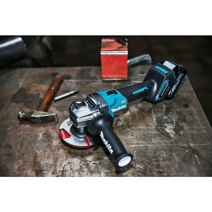 Makita XGT 40V max. Akku-Winkelschleifer GA008GM201 - 2 Akkus, 4 Ah, Durchmesser Scheibe: 125 mm - Blaue und schwarze Makita Akku-Winkelschleifer mit Trennscheibe, auf einer Metallwerkbank neben einem Hammer.