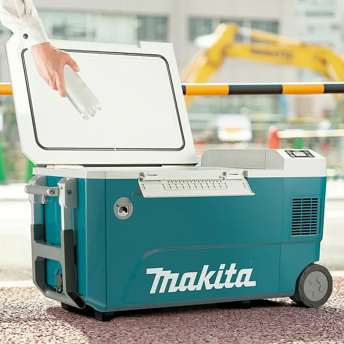 Makita Akku-Kühlbox zum Kühlen & Warmhalten CW002GZ01 - Ohne Akku, 50 l - Türkise und weiße Makita Kühl-/Wärmebox mit Rädern, geöffnet, eine Hand legt eine Wasserflasche hinein, auf einer Baustelle.