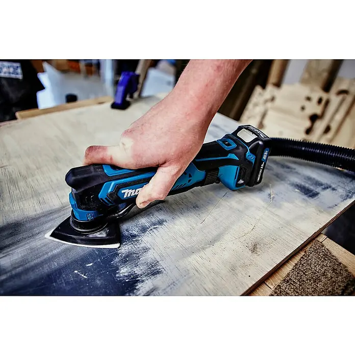 Makita CXT 12V max. Akku-Multifunktionswerkzeug TM30DZ - 12 V, Ohne Akku - Blau-schwarzer Makita Akku-Multifunktionsschleifer in einer Hand, der Holz schleift. Akku und Absaugschlauch sind angeschlossen.