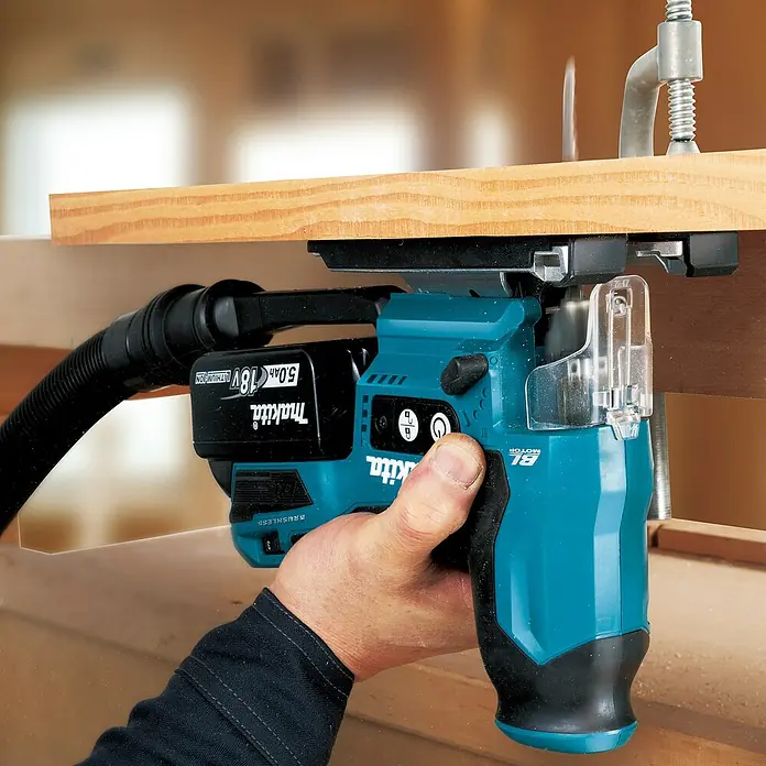 Makita LXT 18V Akku-Pendelhubstichsäge DJV185Z - 18 V, Ohne Akku, Leerlaufhubzahl: 800 /min - 3.000 /min - Blauer und schwarzer Makita Akku-Fräser, von einer Hand gehalten, bearbeitet Holz. Mit Absaugschlauch.