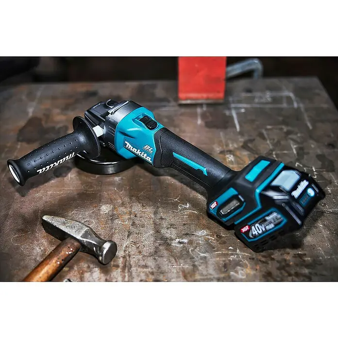 Makita XGT 40V max. Akku-Winkelschleifer GA008GM201 - 2 Akkus, 4 Ah, Durchmesser Scheibe: 125 mm - Ein schwarzer und türkiser Makita Akku-Winkelschleifer mit Zusatzgriff, auf einer Metallwerkbank neben einem Hammer.