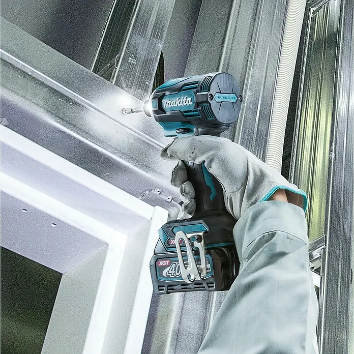 Makita XGT 40V max. Akku-Schlagschrauber TD001GD201 - 40 V, 2 Akkus, 2,5 Ah - Eine behandschuhte Hand verwendet einen türkisfarbenen und schwarzen Makita Schlagschrauber mit einem 40V XGT Akku, um eine Schraube in einen Metallrahmen zu treiben.