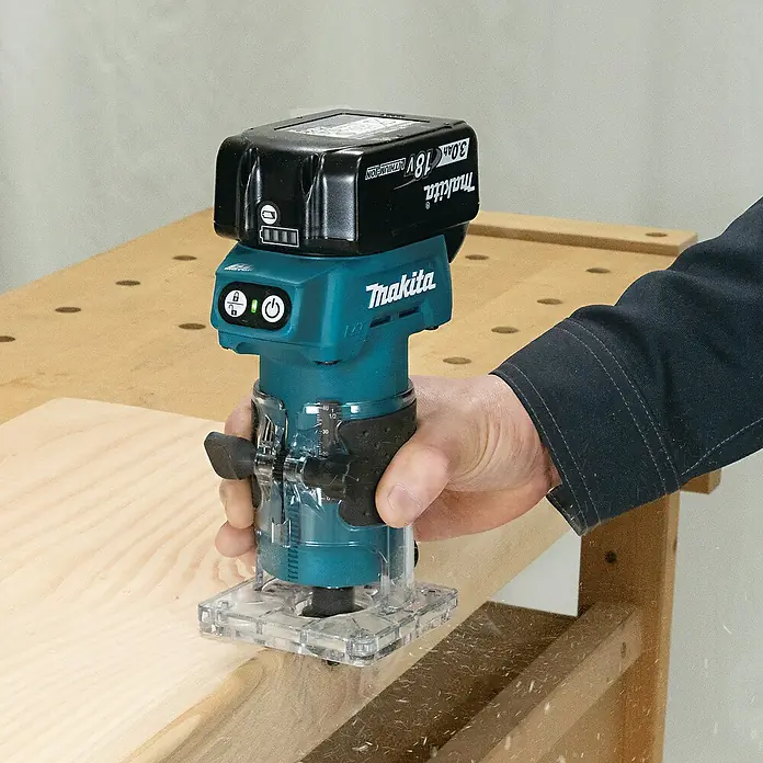 Makita LXT 18V Akku-Kantenfräser DRT52Z - 18 V, Ohne Akku, Leerlaufdrehzahl: 30.000 U/min - Eine Person fräst Holz mit einem petrolfarbenen und schwarzen Makita Akku-Fräser.