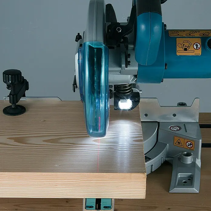 Makita Kapp- & Gehrungssäge LS0815FLN - 1.400 W, Durchmesser Sägeblatt: 216 mm, 0 U/min - 5.000 U/min - Eine teal- und grau-farbene Kapp- und Gehrungssäge sägt ein Holzbrett. Ein weißes LED-Licht und eine rote Laserlinie zeigen den Schnittweg an.