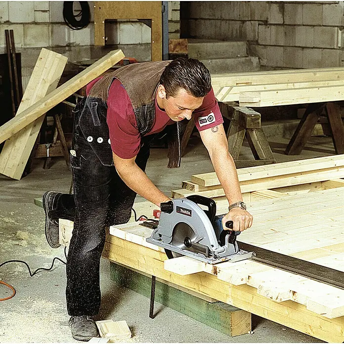Makita Handkreissäge 5103R - 2.100 W, Durchmesser Sägeblatt: 270 mm, Schnitttiefe bei 90 °: 100 mm - Mann bedient eine grau-schwarze Kreissäge, um Holzbretter auf einer Werkbank zu schneiden.