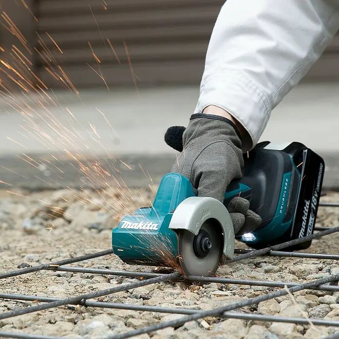 Makita LXT 18V Amoladora angular de batería DMC300Z - 18 V, Sin batería - Una persona utiliza una amoladora angular Makita turquesa y negra con una cuchilla giratoria para cortar varillas, generando chispas brillantes.
