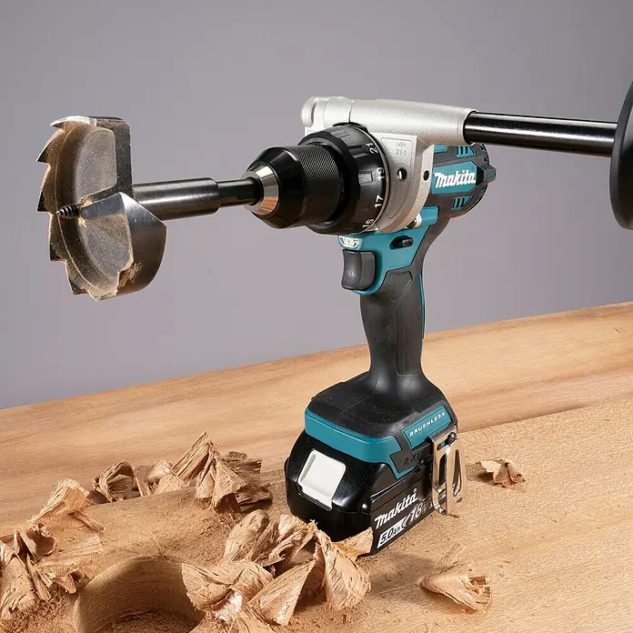 Makita LXT 18V Akku-Bohrschrauber DDF492RTJ - 18 V, 2 Akkus, 130 Nm - Makita Akku-Bohrschrauber mit großem Bohrer, der in Holz bohrt, umgeben von Spänen. Türkis-schwarzes Werkzeug mit silbernen Akzenten.