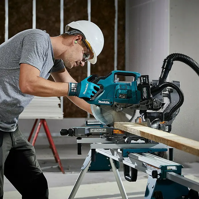Makita XGT 40V max. Akku-Kapp- & Gehrungssäge LS002GZ01 - 40 V, Ohne Akku, 4.800 U/min - Mann in Schutzausrüstung schneidet Holz mit einer türkis-schwarzen Makita Kappsäge auf einer Baustelle.