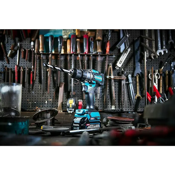 Makita XGT 40V max. Akku-Schlagbohrschrauber HP001GD201 - 40 V, 2 Akkus, 2,5 Ah, 41 Nm - Türkis-schwarze Makita Akku-Bohrmaschine mit Bohrer und 40V XGT Akku, in einer Werkstatt unter verschiedenen Werkzeugen.