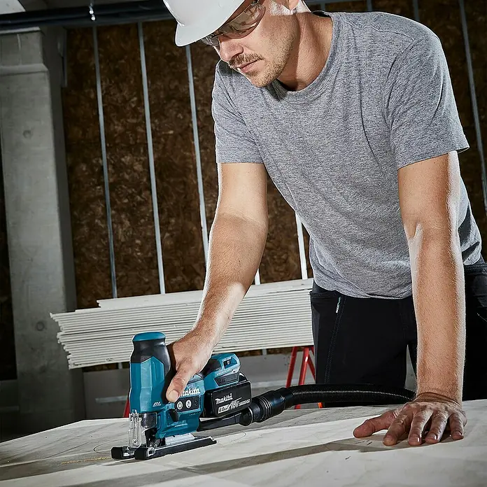 Makita LXT 18V Akku-Pendelhubstichsäge DJV185Z - 18 V, Ohne Akku, Leerlaufhubzahl: 800 /min - 3.000 /min - Mann benutzt eine teal-schwarze Makita Akku-Stichsäge mit Staubabsaugung, um ein rundes Stück Holz zu schneiden.