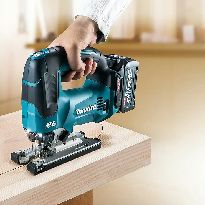 Makita XGT 40V max. Akku-Pendelhubstichsäge JV002GZ - 40 V, Ohne Akku, 0 /min - 3.500 /min - Blaue und schwarze kabellose Makita Stichsäge, von einer Hand gehalten, sägt ein Holzbrett. Mit 40V XGT Li-Ionen Akku.