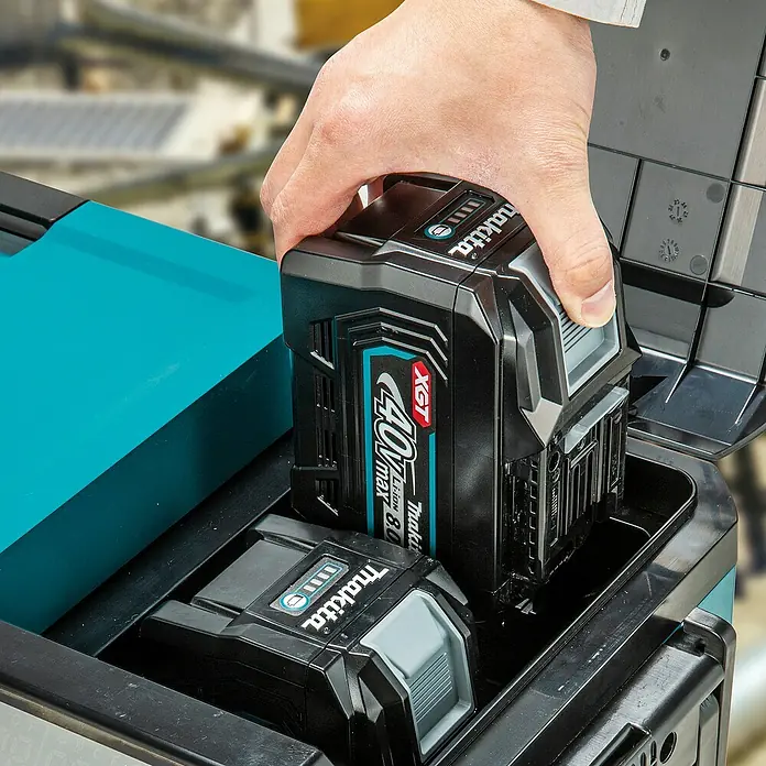 Makita Akku-Kühlbox zum Kühlen & Warmhalten CW004GZ - 18 V, Ohne Akku, 29 l - Hand legt einen Makita XGT 40V max Akku in ein schwarz-türkises Fach, ein weiterer Akku ist sichtbar.
