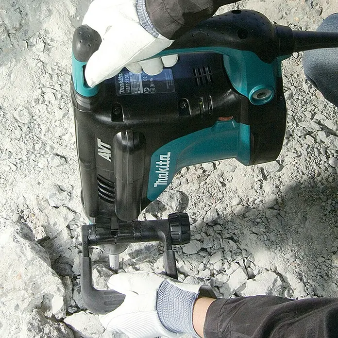 Makita Abbruchhammer HM1213C - 1.510 W, 18,6 J, SDS-Max-Aufnahme - Eine Person mit weißen Handschuhen bedient einen türkis-schwarzen Makita Abbruchhammer, um Beton zu zerkleinern.