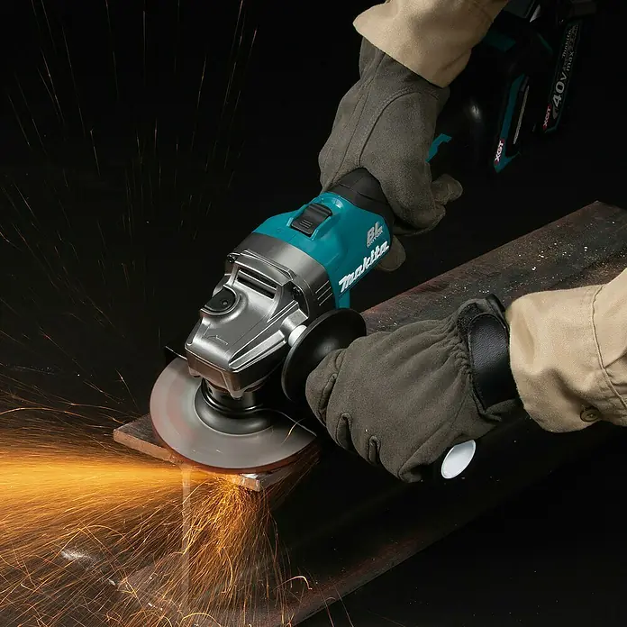 Makita XGT 40V max. Akku-Winkelschleifer GA008GM201 - 2 Akkus, 4 Ah, Durchmesser Scheibe: 125 mm - Teal- und silberfarbener Makita Winkelschleifer, von behandschuhten Händen gehalten, schneidet Metall und erzeugt helle orangefarbene Funken.