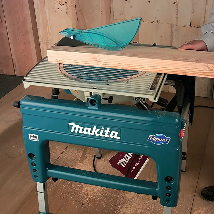 Makita Tischkreissäge & Kapp-Gehrungssäge LF1000 - 1.650 W, Durchmesser Sägeblatt: 260 mm - Eine türkisfarbene Makita Flipper Tischkreissäge schneidet ein Holzbrett, bedient von einer Hand. Sägespäne am Boden zeigen aktive Nutzung.