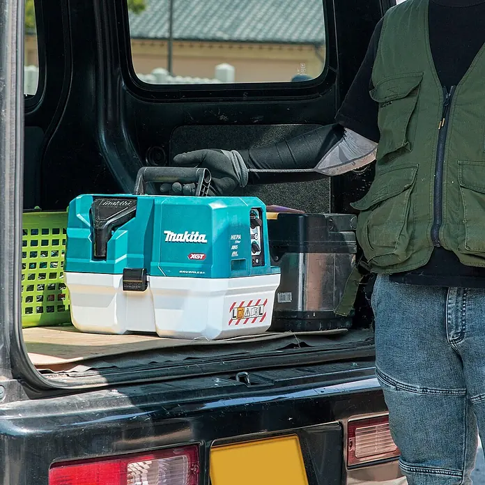 Makita XGT 40V max. Akku-Nass-Trockensauger VC013GLZ03 - 40 V, Ohne Akku, Behältervolumen: 7,5 l - Türkis-weißer Makita XGT Staubsauger mit HEPA-Filter wird in ein Fahrzeug geladen.