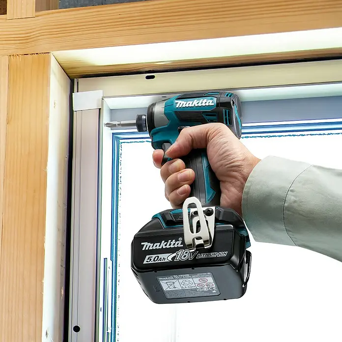 Makita LXT 18V Akku-Schlagschrauber DTD173Z - 18 V, Ohne Akku - Eine Hand hält einen Makita Schlagschrauber mit einem 5.0Ah 18V Akku, der eine Schraube in einen weißen Fensterrahmen eindreht.