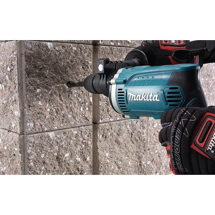 Makita Schlagbohrmaschine HP1631KX3 - 710 W, Schnellspannbohrfutter - Teal- und schwarzer Makita Bohrhammer, von behandschuhten Händen gehalten, bohrt in eine graue Betonwand.