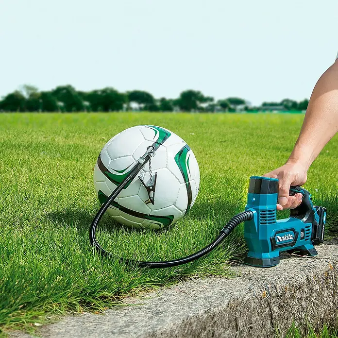 Makita CXT 12V max. Akku-Kompressor MP100DZ - 12 V, Li-Ionen, Ohne Akku, Max. Druck: 8,3 bar - Eine Hand hält einen türkis-schwarzen Makita Kompressor, der einen weißen Fußball aufpumpt.