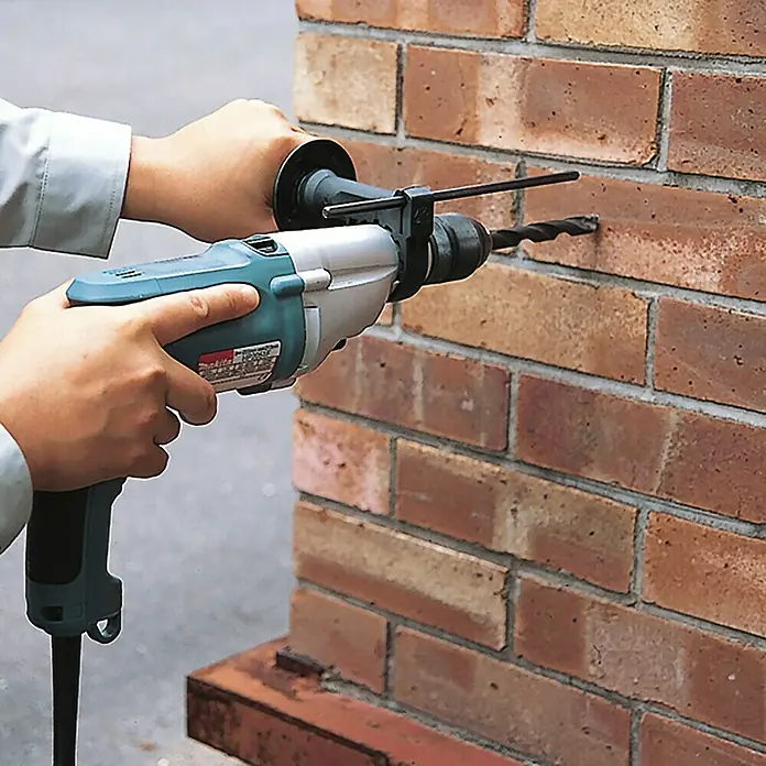 Makita Schlagbohrmaschine HP2051J - 720 W, Schnellspannbohrfutter - Person bohrt mit einem türkis-silbernen Bohrhammer ein Loch in eine rote Ziegelwand.