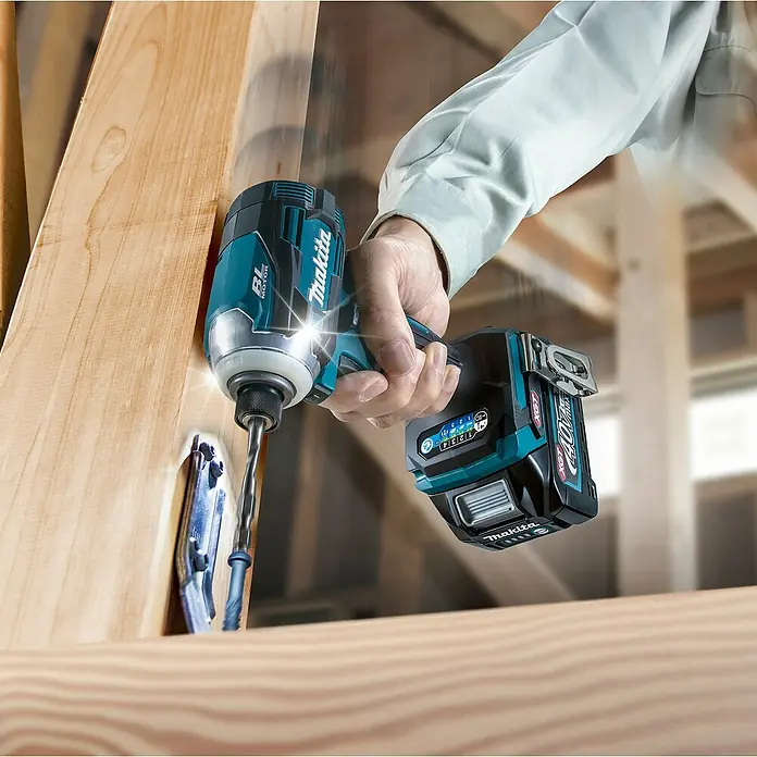 Makita XGT 40V max. Akku-Schlagschrauber TD001GD201 - 40 V, 2 Akkus, 2,5 Ah - Eine Hand bedient einen türkis-schwarzen Makita Schlagschrauber mit 40V Akku, der in einen hellen Holzbalken schraubt.