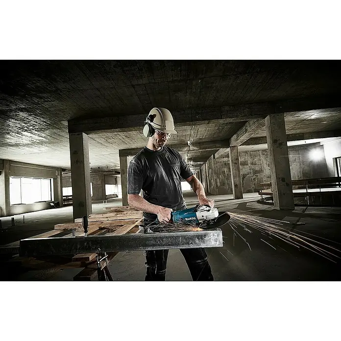 Makita Elektro-Winkelschleifer GA9020RFK3 - 2.200 W, Durchmesser Scheibe: 230 mm, Leerlaufdrehzahl: 6.600 U/min - Arbeiter in Schutzausrüstung verwendet blauen Makita Winkelschleifer, um einen Metallträger zu schneiden, Funken sprühen auf Baustelle.