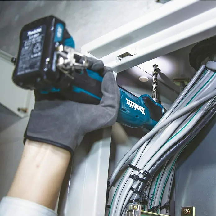Makita CXT 12V max. Akku-Winkelbohrmaschine DA332DSYJ - 12 V, 1 Akku - Eine behandschuhte Hand hält eine türkis-schwarze Makita Akku-Bohrmaschine und bohrt ein Loch in einen Schaltschrank in der Nähe gebündelter Kabel.