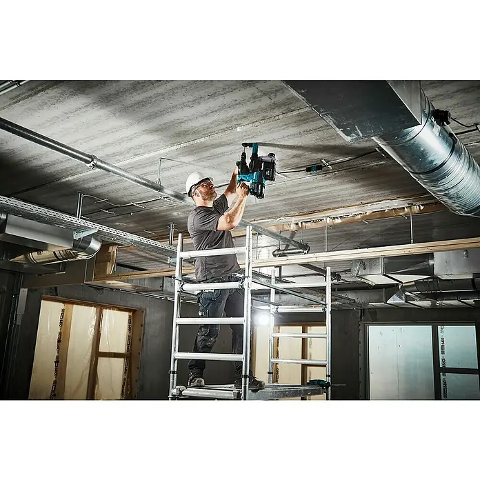 Makita XGT 40V max. Akku-Kombihammer HR004GM201 - 40 V, 2 Akkus, 2,9 J - Mann auf Gerüst bohrt mit blauem Akku-Bohrhammer und Staubabsaugung in Betondecke.