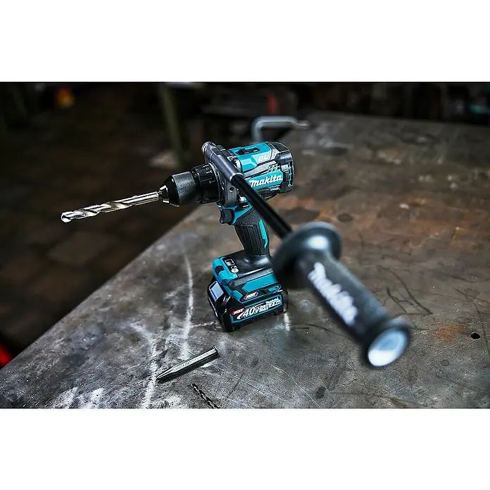 Makita XGT 40V max. Akku-Schlagbohrschrauber HP001GD201 - 40 V, 2 Akkus, 2,5 Ah, 41 Nm - Türkis-schwarze Makita Akku-Bohrmaschine mit Bohrer und Zusatzhandgriff auf dunkler Metallwerkbank mit Körner und weiterem Bohrer.