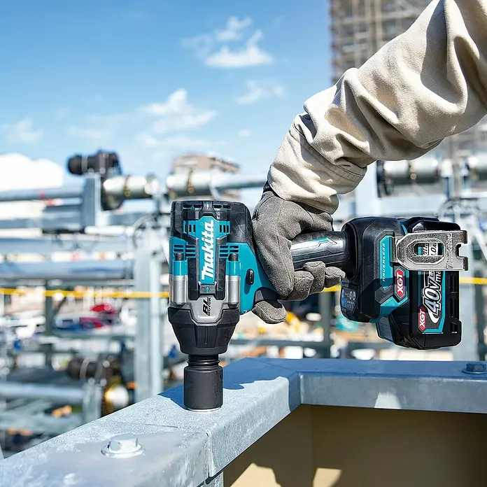Makita XGT 40V max. Akku-Schlagschrauber TW008GZ - 40 V, Ohne Akku, 760 Nm - Ein Arbeiter hält einen schwarz-türkisen Makita XGT 40V Schlagschrauber mit Nuss auf einem Metallträger auf einer Baustelle.