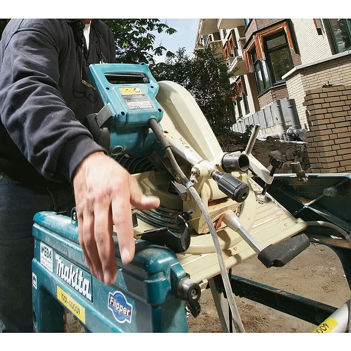 Makita Tischkreissäge & Kapp-Gehrungssäge LF1000 - 1.650 W, Durchmesser Sägeblatt: 260 mm - Eine Person bedient ein blau-beiges Makita Elektrowerkzeug, wahrscheinlich eine Kappsäge, auf einer Baustelle.