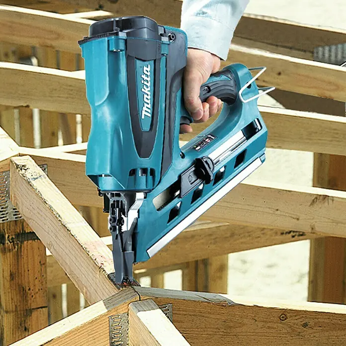Makita Akku-Gasnagler GN900SE - 7,2 V, 2 Akkus, Länge Nagel: 50 mm - 90 mm - Türkise und schwarze Makita Nagelpistole, von einer Hand gehalten, die einen Nagel in Holzrahmen schlägt.