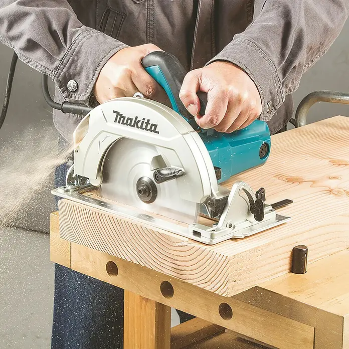 Makita Handkreissäge HS7611 - 1.600 W, Durchmesser Sägeblatt: 190 mm - Eine Person sägt mit einer Makita-Kreissäge ein Holzbrett, wobei Sägespäne entstehen.
