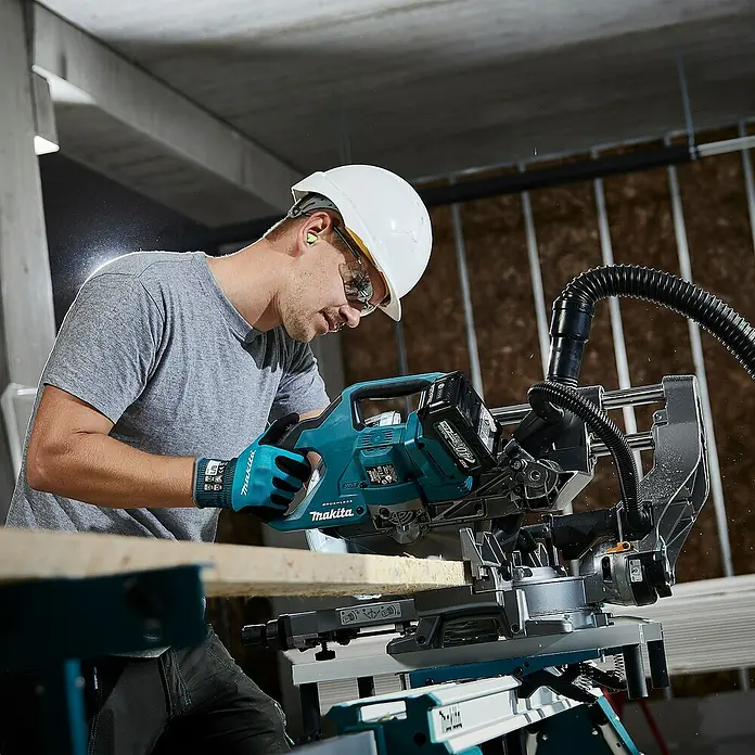 Makita XGT 40V max. Akku-Kapp- & Gehrungssäge LS002GZ01 - 40 V, Ohne Akku, 4.800 U/min - Ein Arbeiter mit Schutzkleidung benutzt eine teal-schwarze Makita XGT Akku-Kappsäge, um einen Holzbalken zu schneiden.