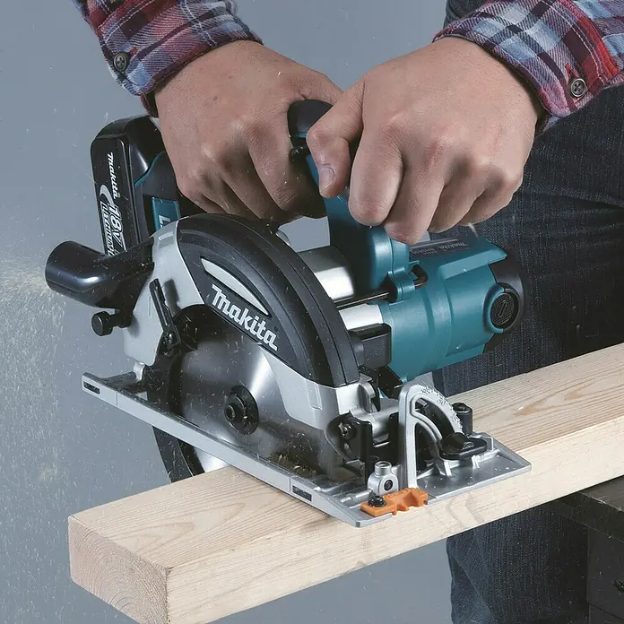 Makita LXT 18V Akku-Handkreissäge DHS630Z - 18 V, Ohne Akku, Leerlaufdrehzahl: 3.100 U/min - Person sägt mit einer blaugrünen und silbernen Makita Akku-Kreissäge ein helles Holzbrett, Späne fliegen.