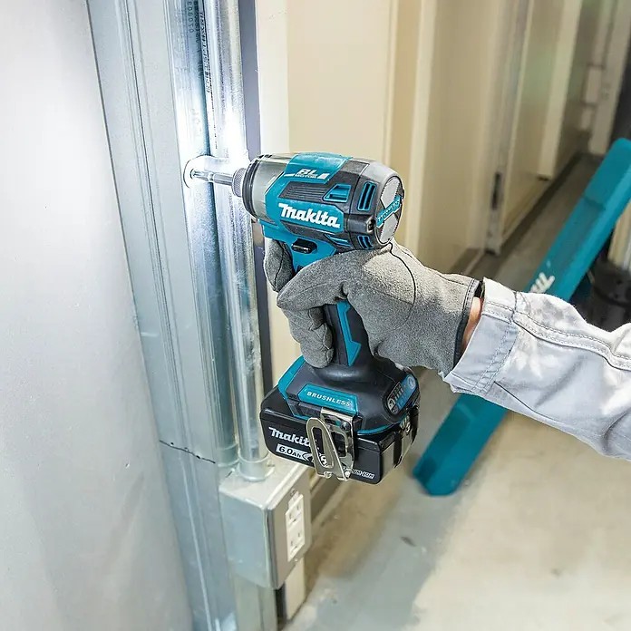 Makita LXT 18V Akku-Schlagschrauber DTD173Z - 18 V, Ohne Akku - Behandschuhte Hand befestigt mit einem schwarz-türkisen Makita Schlagschrauber und 6.0Ah Akku eine Schraube in einem Metallständer.