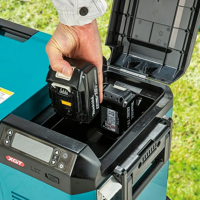 Makita Akku-Kühlbox zum Kühlen & Warmhalten CW004GZ - 18 V, Ohne Akku, 29 l - Hand steckt einen schwarzen Makita 18V Akku in eine türkis-schwarze tragbare Powerstation mit Digitalanzeige.