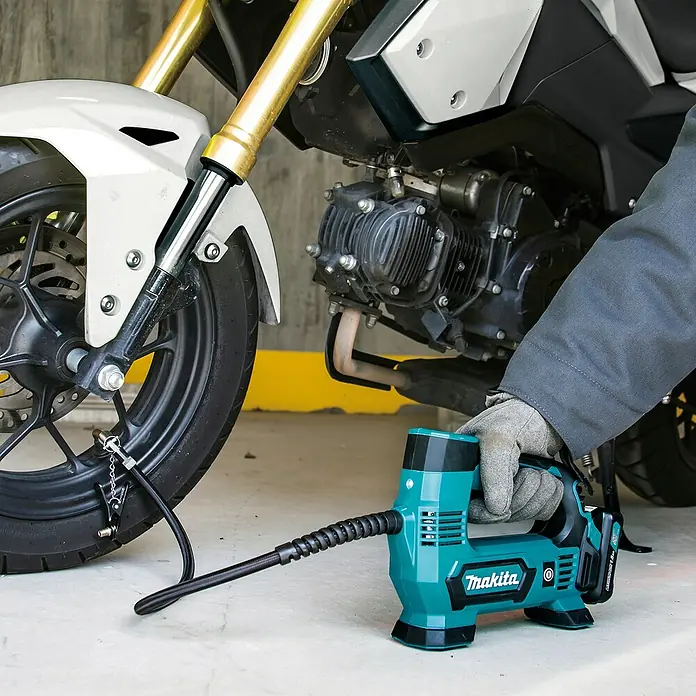 Makita CXT 12V max. Akku-Kompressor MP100DZ - 12 V, Li-Ionen, Ohne Akku, Max. Druck: 8,3 bar - Türkiser und schwarzer Makita Akku-Luftkompressor, von einer behandschuhten Hand gehalten, bläst einen Motorradreifen auf.